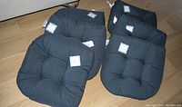 Six charcoal colored outdoor seat cushions arranged on floor, all visible with tags attached