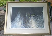 Full photograph of framed limited edition print showing the water surface with reflections, lily pads, and the tree swallow bird in the upper right area. Shows triple matting and muted gold wood frame.