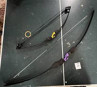 Two Barnett bows lying parallel on a ping pong table showing full bows with mounted bowstrings and colored grips.