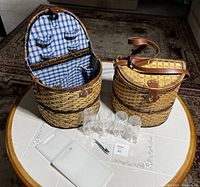 Photo showing two picnic baskets with blue and white checkered interior, two small clear plastic glasses in front, and two white cutting boards placed on a round table.