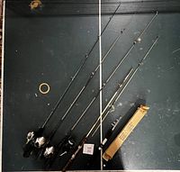 Five fishing rods and reels laid out on flat surface, one boxed folding rod