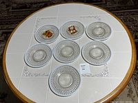 Seven Anchor Hocking Hobnail Moonstone opalescent glass dinner plates arranged on a circular table with white tiled surface, showing the hobnail textured rim and sunburst center design.