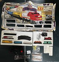 Overall view of the train set with box top laid open and all main components in styrofoam tray including locomotive, train cars, tracks, controller, and accessories.