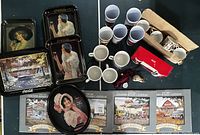 Top view of lot showing metal trays, mugs, cups, calendars, figurines and plush toy arranged on table.
