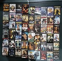 Photo showing a large collection of DVD movies laid out on a surface, including visible titles such as Alpha Dog, Nancy Drew, Shutter Island, Hunger Games, Lord of the Rings, Bourne Identity, The Princess Bride, Sherlock Holmes, Harry Potter, and others.