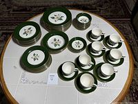 Full lot view showing plates, bowls, cups and saucers arranged on a table, highlighting the green jade border with floral design.