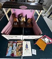 Front and aerial view of wooden pink and white Our Generation house barn with two toy horses inside, horse tack, three American Girl books and small wooden doll chair.