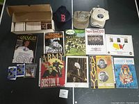 Box filled with football and other trading cards, two sealed 1990 Pro Set hockey card packs, sports hats, Sports Illustrated and Army football magazines, and NFL game program booklets.