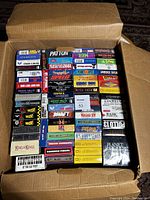 Overhead photo of open cardboard box filled with vertically arranged VHS tapes showing spines with various titles.