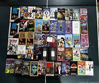 Photo showing 46 VHS movie tapes, arranged covering partial reflective surface. Titles include Back to the Future, Star Trek, Jurassic Park, The Witches of Eastwick, Home Alone series, and others.