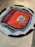 Round wool rug showing abstract modern design in red, gray, black, yellow and blue with an outer gray border and black accents.