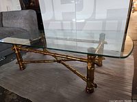 View of the full coffee table showing the glass top and gold-colored bamboo-inspired metal frame with crossbar support underneath.
