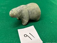 Front and side view of the small gray stone Inuit bear carving on green felt background.