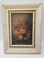 Front view of old oil on canvas still life painting with cream-colored decorative frame that shows some wear and chipping.