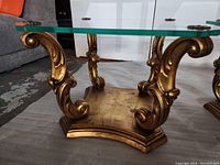 View of one coffee table showing ornate gold scrollwork base and clear beveled glass top
