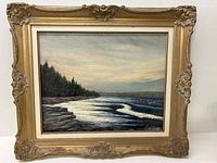 Full view of the oil painting on ornate carved gold-toned frame showing the coastal scene with trees, rocky shore and water.