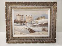 Framed full view of an oil painting showing a winter landscape with buildings and snow-covered hills under an overcast sky.