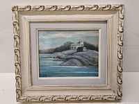 Full view of the framed oil painting showing the coastal church scene with water and rocky terrain.