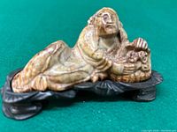 Side view of the carved Chinese figure reclining on a carved base highlighting the detail of the figure and the base.