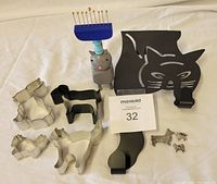 Full view of the lot including black metal cat-shaped clothes hanger, four metal cookie cutters shaped as animals, gray cat figurine with blue comb, and small metal animal jewelry pieces.
