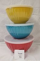 Stacked set of three melamine mixing bowls in yellow, blue, and red with white lids, showing the nested nature of the set.