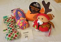 Four dog toys arranged on a beige surface including a transparent bone with apple patterns, a multicolor plush fish, an orange pumpkin plush, and a festive reindeer plush toy.
