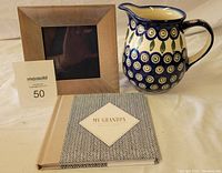 Photo showing the frame, pitcher, and memory book on a beige cloth background with a MaxSold lot card.