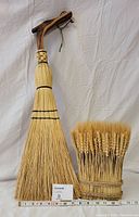 Full view of both items together showing the broom and the harvest wheat bouquet with a measurement ruler below