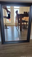 Full view of rectangular mirror with black frame reflecting dining room area and door.