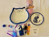 Photo showing two ceramic cat food bowls and a pair of fabric mice toys with feathers and ribbons.