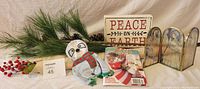 Full lot image showing Christmas decor including glass triptych, Peace on Earth sign, puzzle book, dog toy, and faux pine and berry branches.