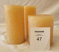 Three Pottery Barn timber scented pillar candles, two taller and narrower and one wider and shorter, displayed against a beige fabric background with MaxSold card.