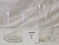 Two clear vases side by side, the taller flared top vase to the right, shorter cylindrical to the left