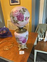 Full view of antique hurricane lamp showing hand painted rose globe and vase base with brass fittings