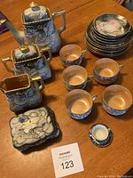 Full tea service arranged on table showing teapot, sugar bowl, creamer, candy dish, plates, cups, saucers and miniature dish with seller tag