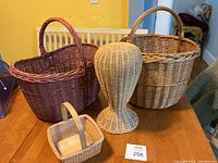 Full view of the four items: two large baskets, small Nantucket basket, and wicker wig holder stand on a wood table.