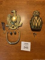 Both brass door knockers with eagle and pineapple designs and all mounting hardware laid out on a wooden surface.