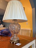 Full view of the vintage crystal table lamp on a wooden table with the cream fabric shade installed.