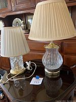 Two crystal table lamps of different heights placed on a reflective dark surface with a front view showing the lamp bases and shades.