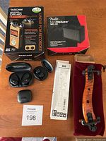 Full view of the electronic and musical accessories lot including boxed Tascam DR-40 recorder and Fender Mini Deluxe MD-20 speaker, wireless earbuds in case, selfie stick, and Artino violin shoulder rest.