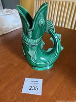 Front and side view of the green Gurgling Cod vase on wood table.