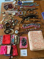 Photo showing full assortment of costume jewelry including necklaces, bracelets, wristwatch, pins, keychains, multiple small fabric jewelry bags and a larger pink/cream floral textured jewelry container.