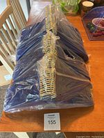Full lot of 100 royal blue hangers sealed in clear plastic wrap on a wooden table.