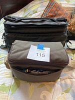 Two camera cases stacked on bed, one Tamtek black case, one soft grey and brown padded case