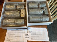 Two boxed sets of four glittery silver remote controlled matchless candles, each set including a remote control and batteries, displayed inside their packaging.