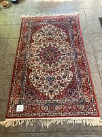 Full view of the oriental rug showing the intricate central medallion and floral border pattern in red, navy, and cream colors with fringed ends.