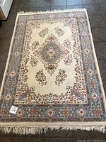 Top view of the 48x74 inch fringed wool hand knotted oriental rug main color cream with light blue and sienna accents.
