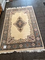 Full view of the oriental rug laid on a dark tile floor showing design, colors, and fringe.