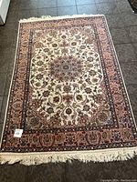 Full view of the rectangular oriental rug showing the elaborate central cream medallion and salmon border with multicolor floral accents and fringed edges.