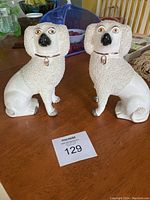 Pair of vintage Old Staffordshire dog figurines on wooden table, showing full bodies and textured fur, white base, collars with tags.
